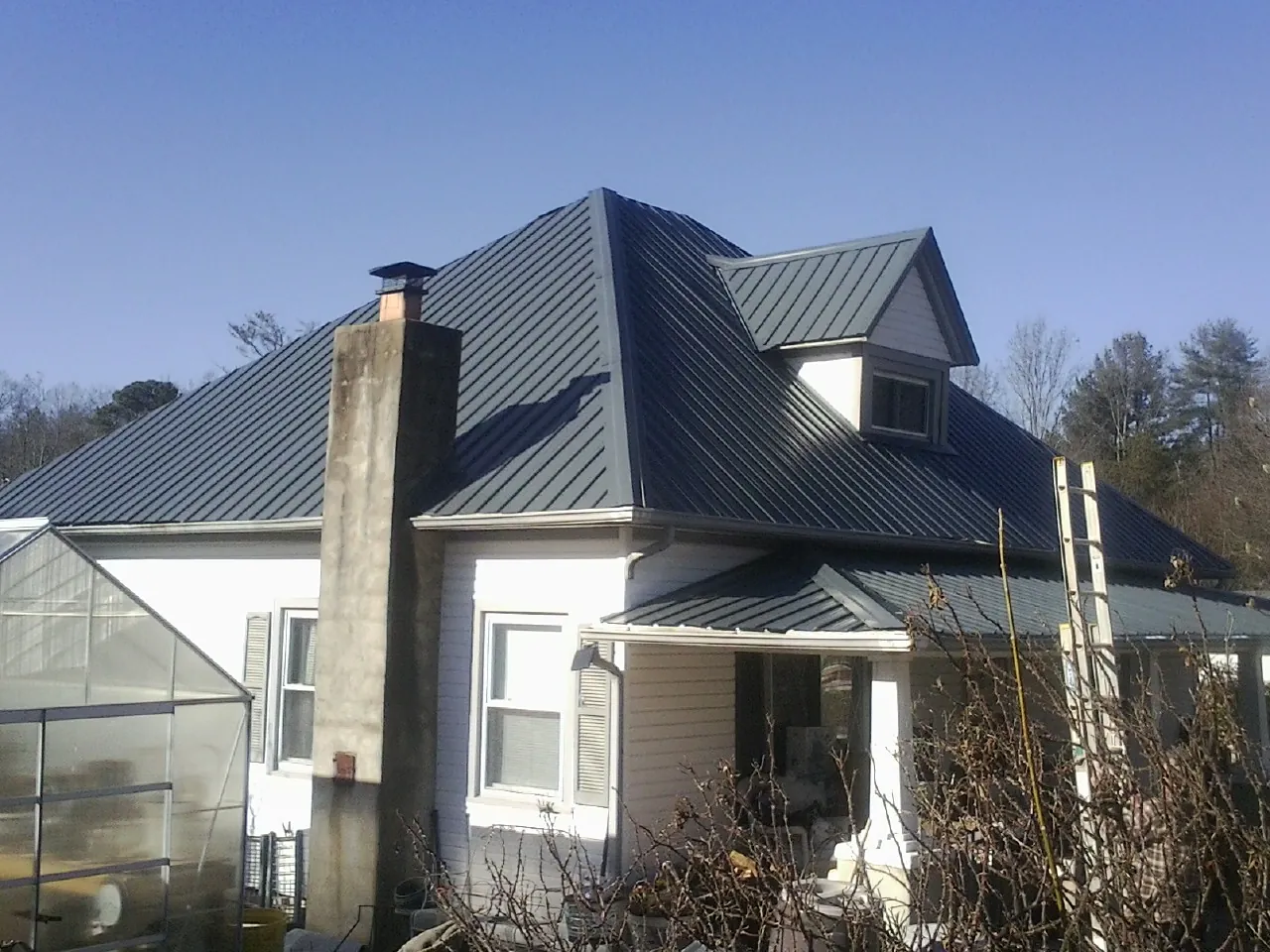 Dark blue standing seam metal roof on a white farmhouse with dormer — Slate & Tile Roof Repair by Roofing Brothers in Mediapolis