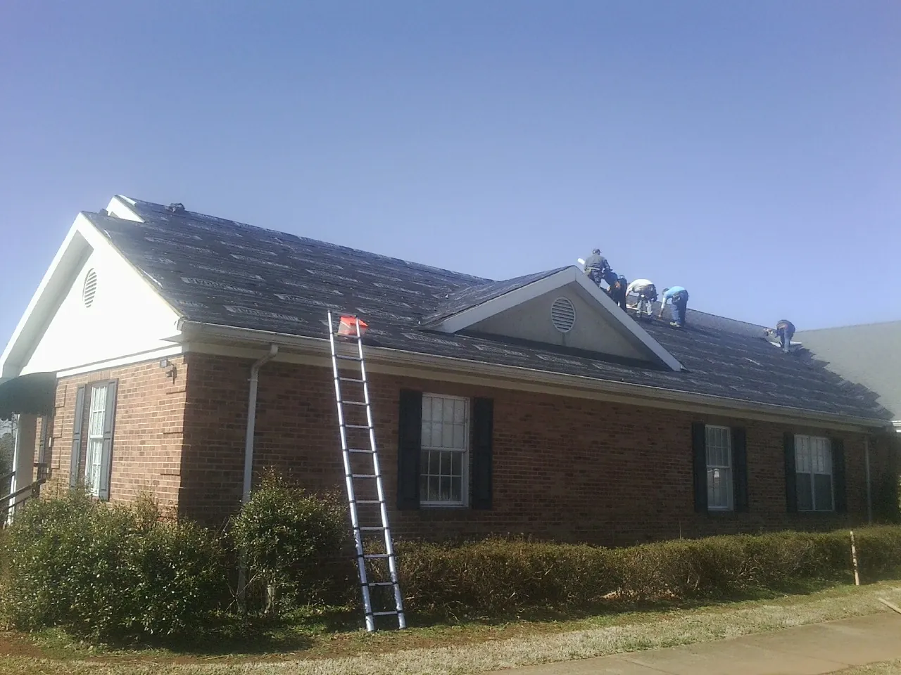 Crew tearing shingles off a brick ranch roof with a ladder set — Metal Roof Repair work by our crew in Mediapolis