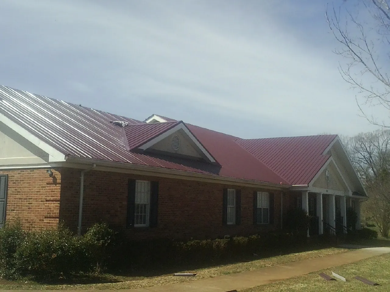 Red metal roof with gabled entries on a long brick building, from a Hail Damage Roof Repair job in Mediapolis