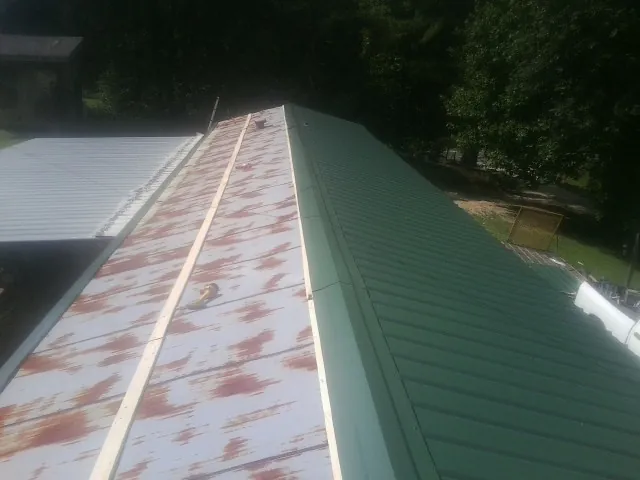Old rusted panels beside newly installed green metal roofing — Wind Damage Roof Repair by Roofing Brothers in Mediapolis