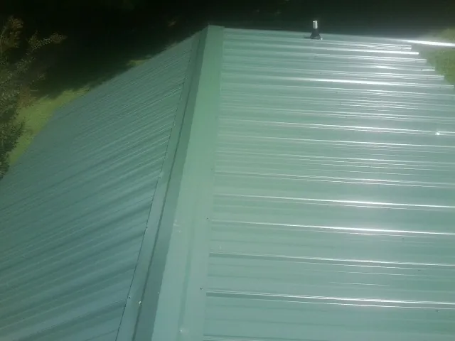 New green metal panels meeting at the ridge of a roof — Flat Roof Repair work by our crew in Mediapolis