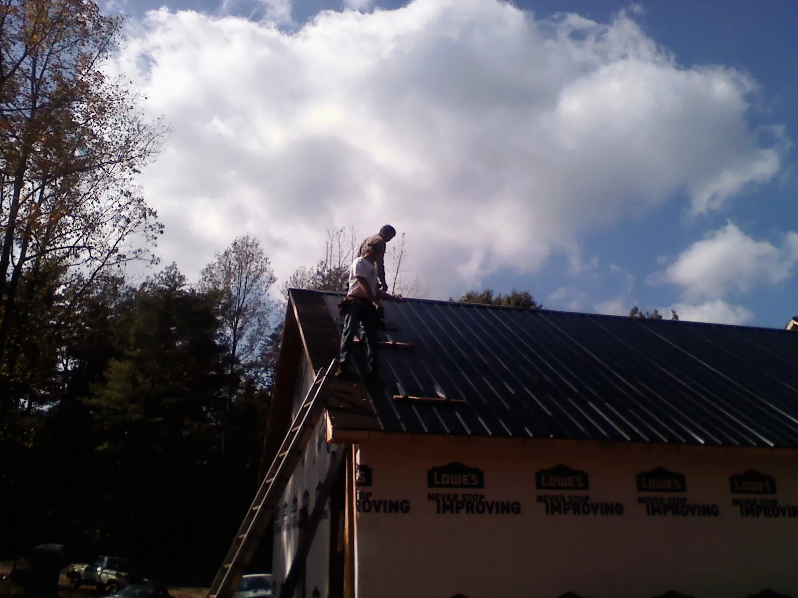 Roofer fastening dark metal panels high against a cloudy sky, from a Roof Inspection job in Mediapolis