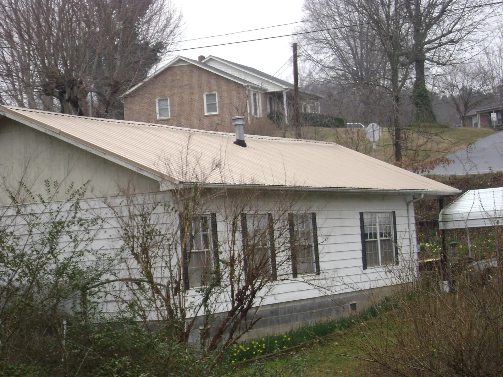 Tan metal roof on a white sided house set into a hillside — Commercial Roofing by Roofing Brothers in Mediapolis