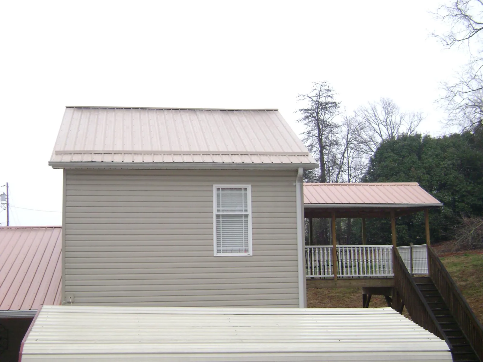 Tan metal roofs on a two story addition and attached porch, from a Roof Replacement job in Mediapolis